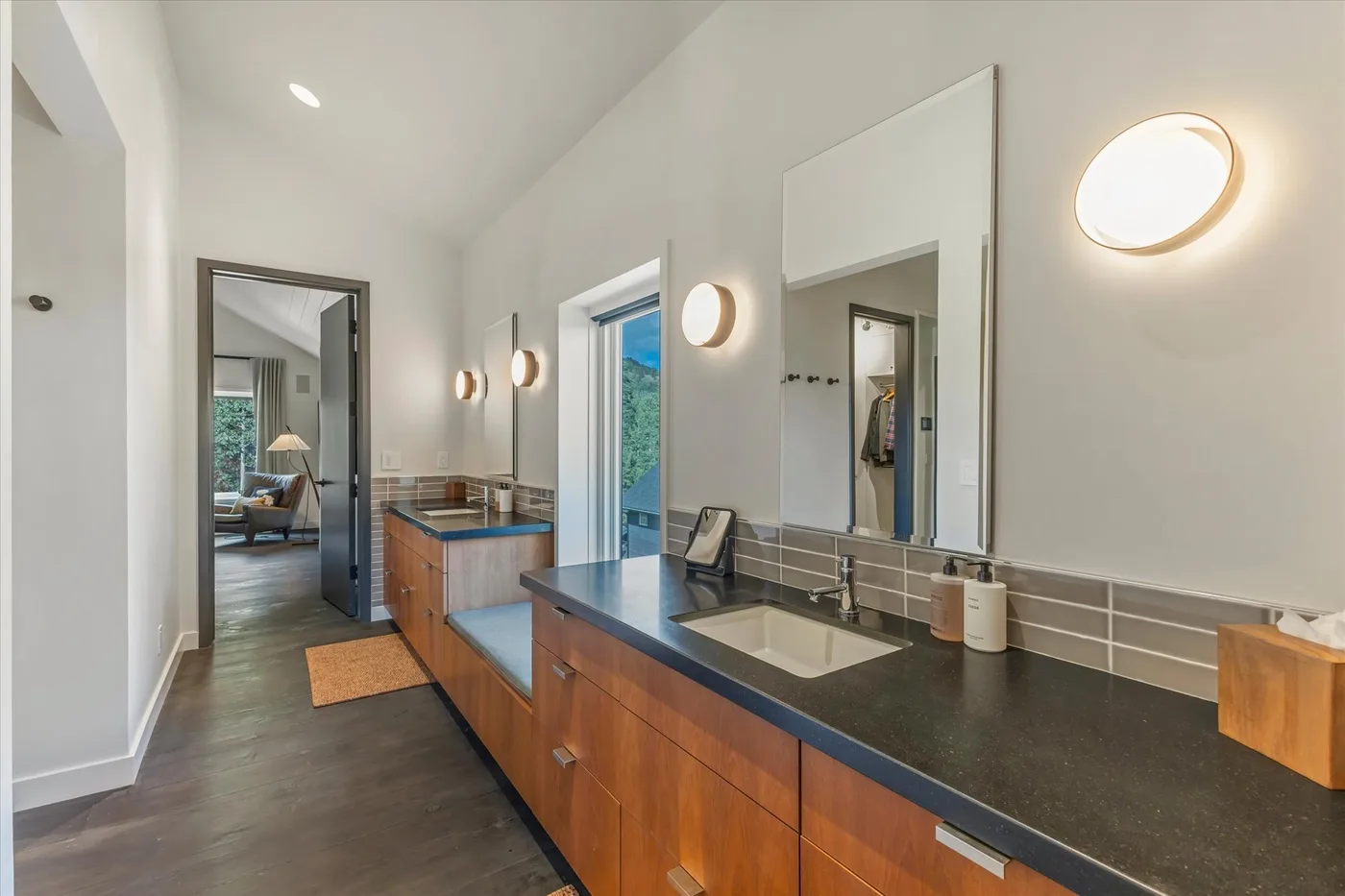 A long bathroom vanity with a dark countertop, mirrors, and wall lights.