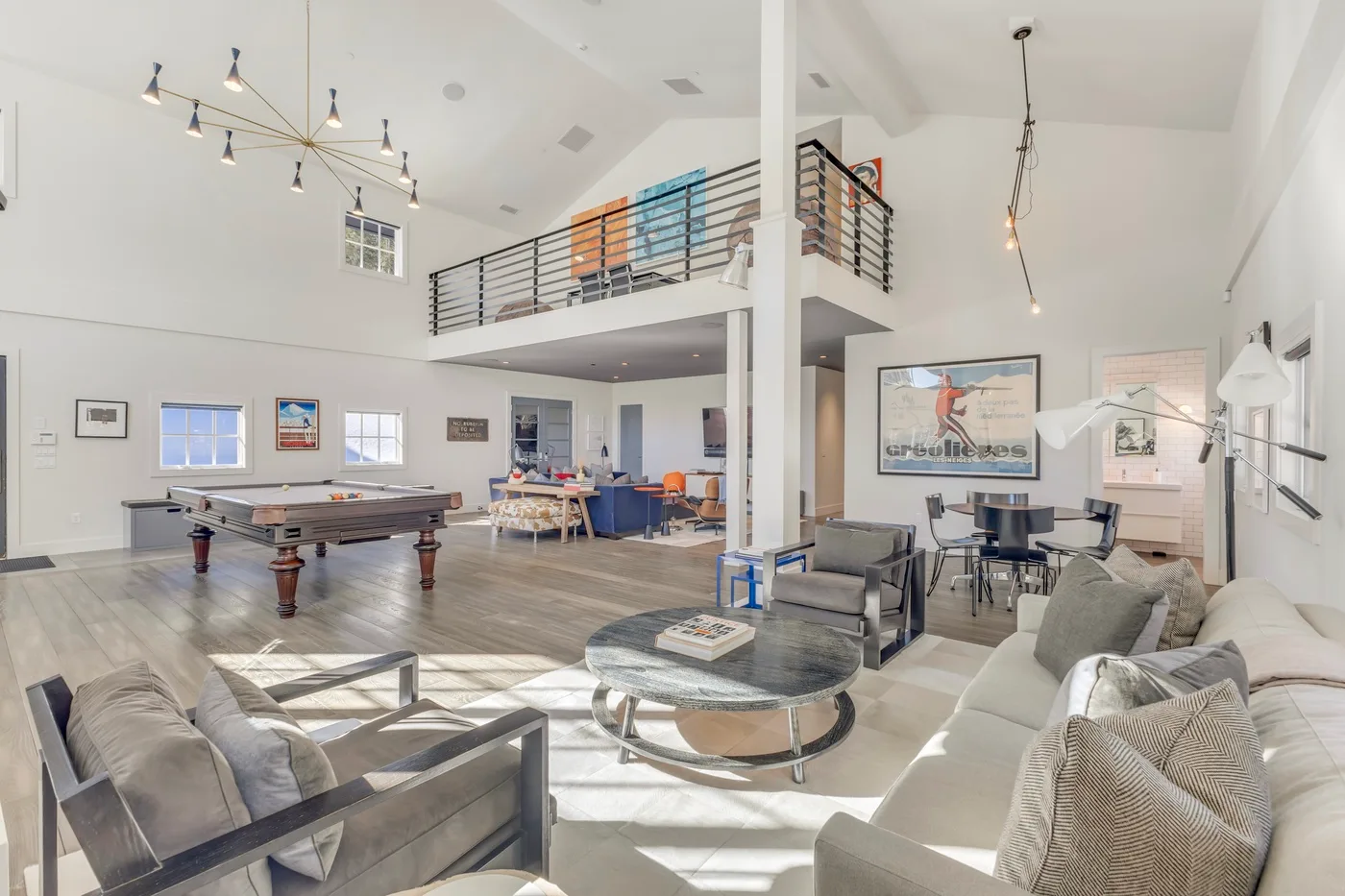 A bright open-plan living area with seating, a pool table, and an upper gallery.