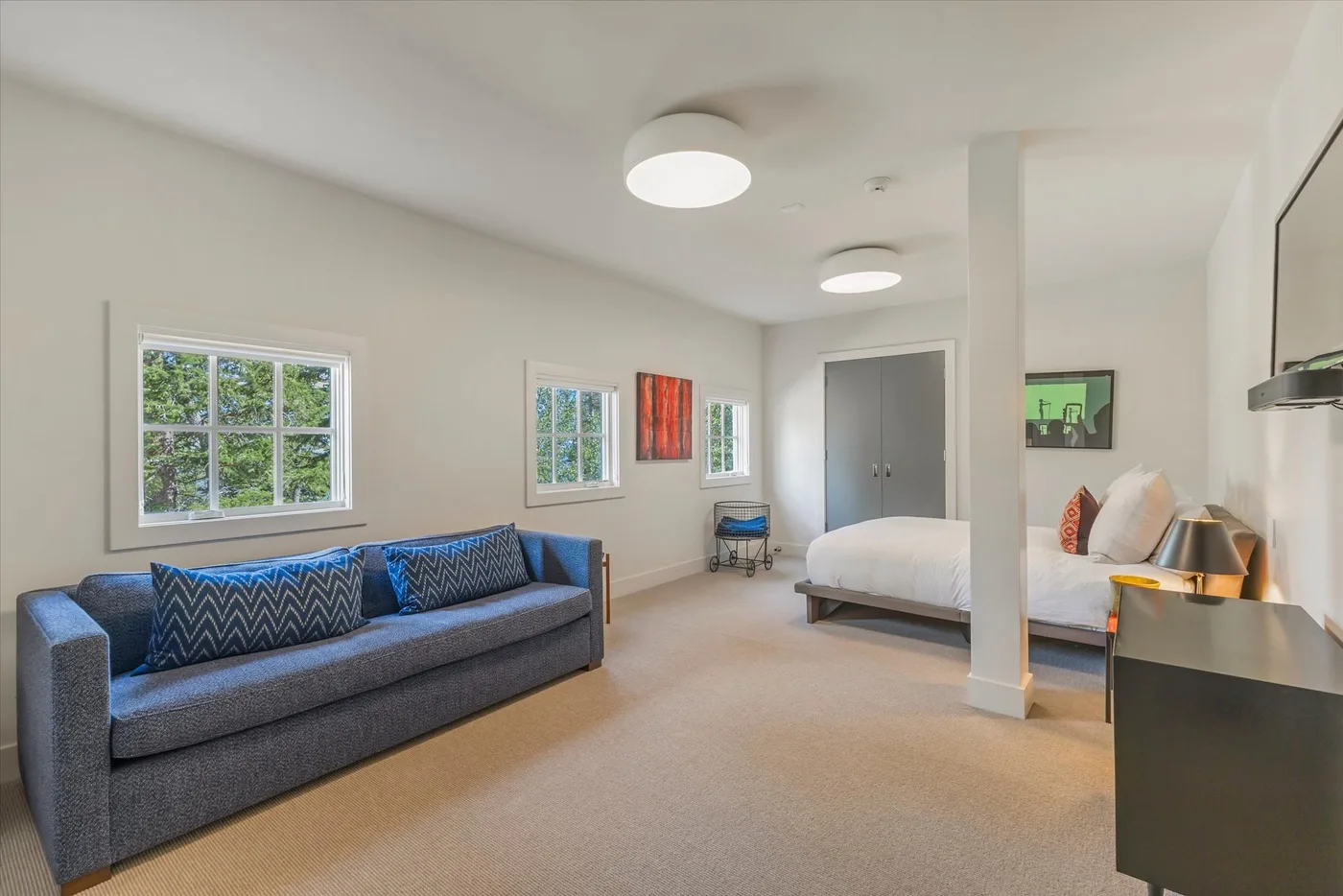 A bright bedroom with a bed, a blue sofa, and windows overlooking greenery.