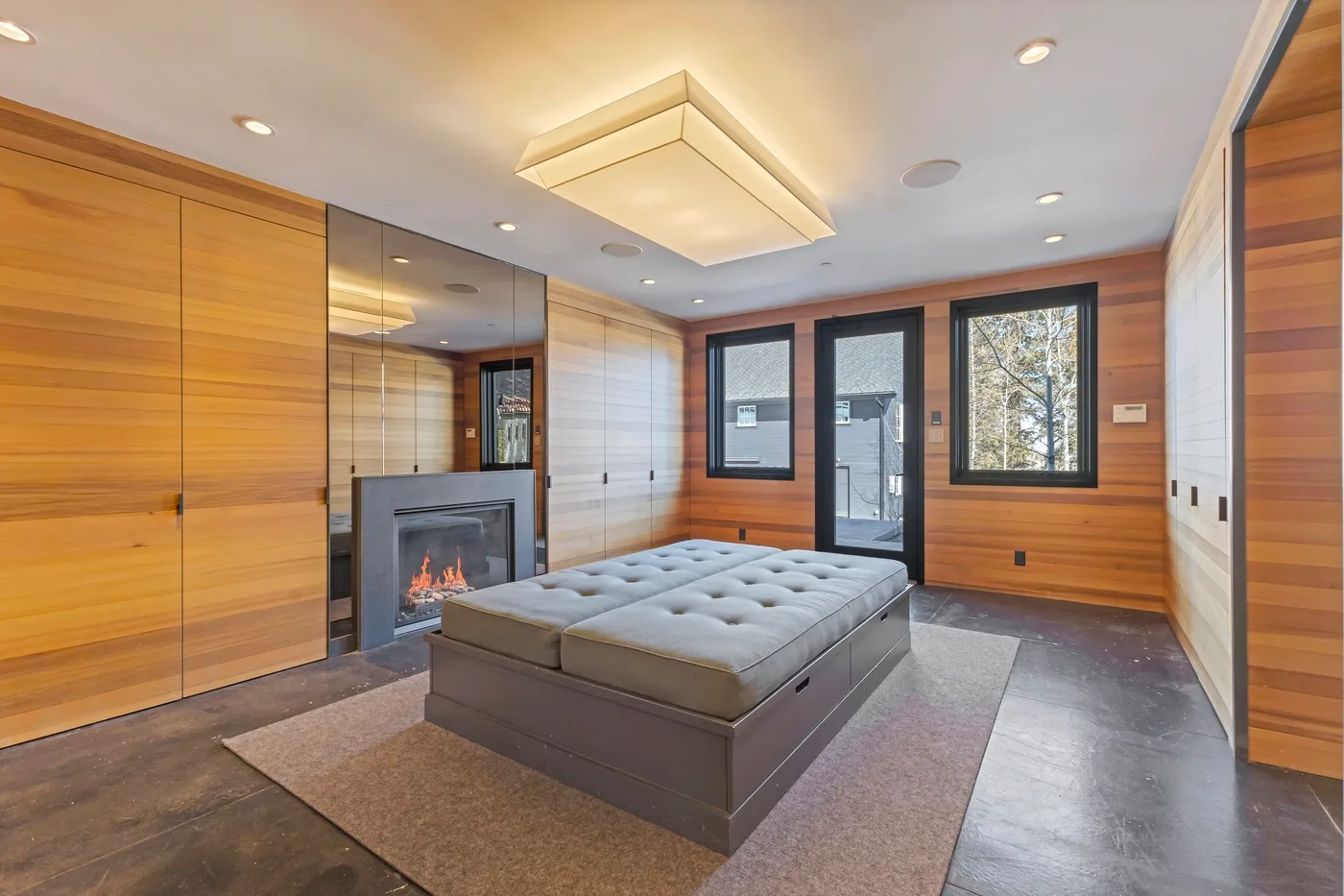 A modern bedroom with a low bed, wood-paneled walls, and a fireplace.