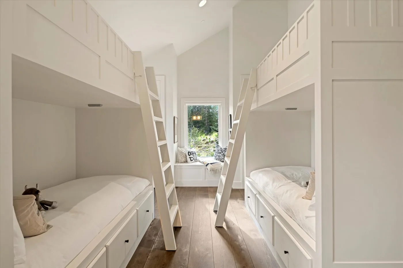 A bright bedroom with two raised beds, ladders, and a window at the far end.