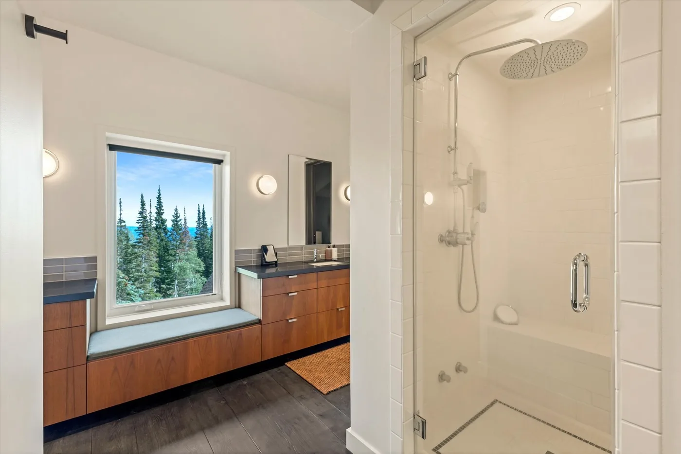 A bright bathroom with a glass shower and a window overlooking trees.