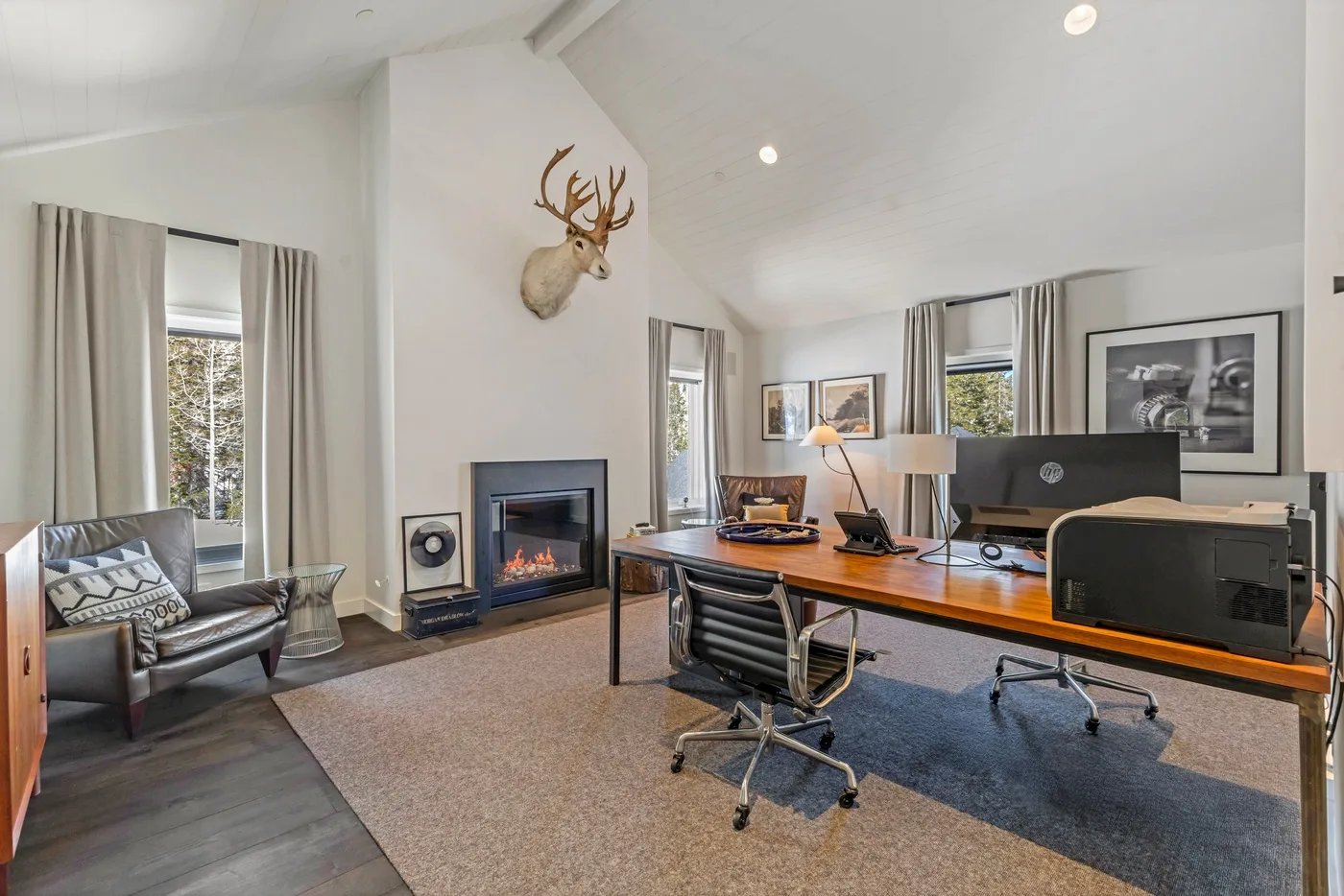 A bright home office with a long desk, office chairs, and a fireplace.