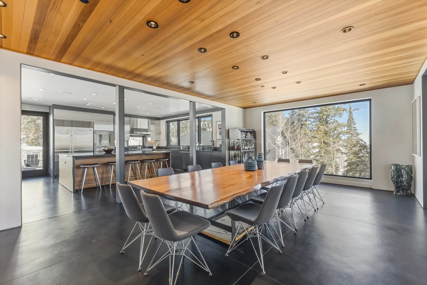 A modern dining area features a long table and a wall of windows.