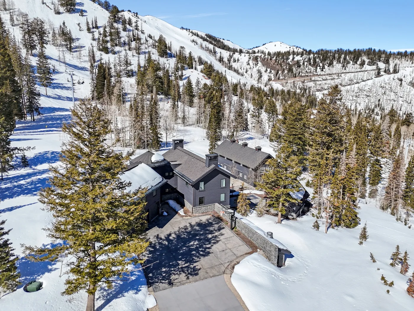 Snow-covered mountain lodge surrounded by evergreen trees and ski slopes.