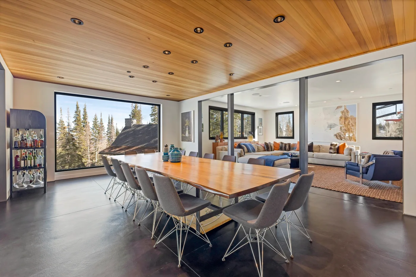 A dining area with a long table and chairs opens onto a living room.