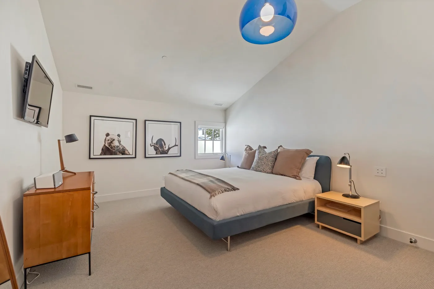A bright bedroom with a neatly made bed and framed artwork on the walls.