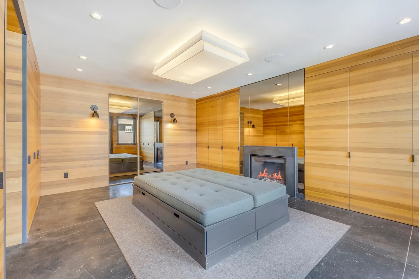 A modern bedroom with a low bed, wood-paneled walls, and a fireplace.