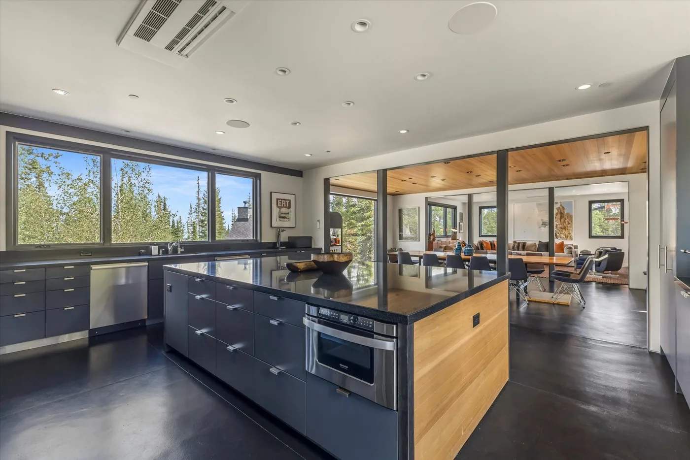 A modern kitchen with a central island opens into a bright living and dining area.