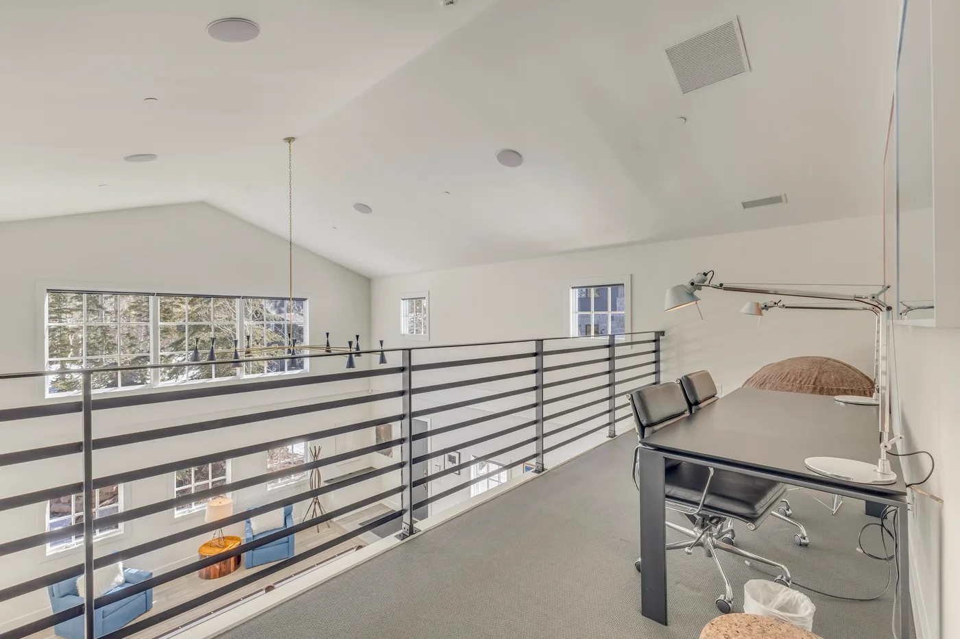 A bright loft workspace overlooks a lower level through a black metal railing.