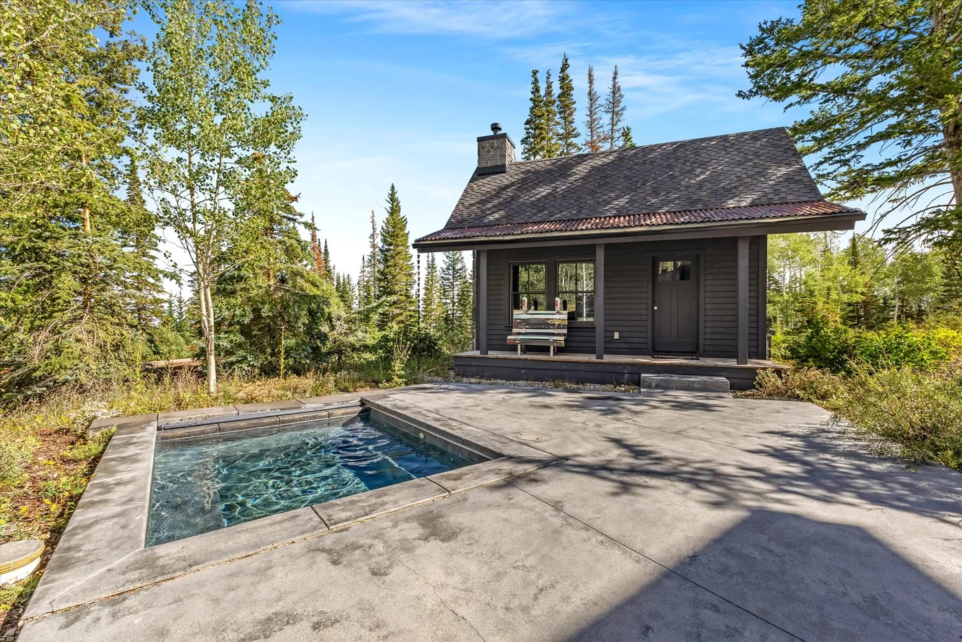 A small cabin beside an outdoor swimming pool, surrounded by trees.