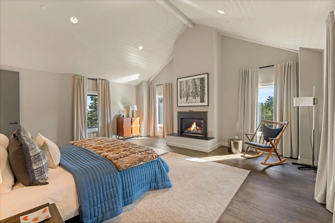 A bedroom with a large bed, a fireplace, and tall windows.
