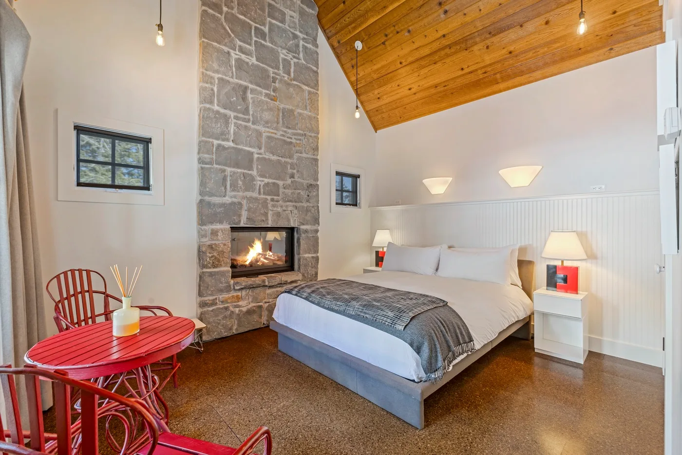 A bedroom with a bed beside a stone fireplace and red seating.