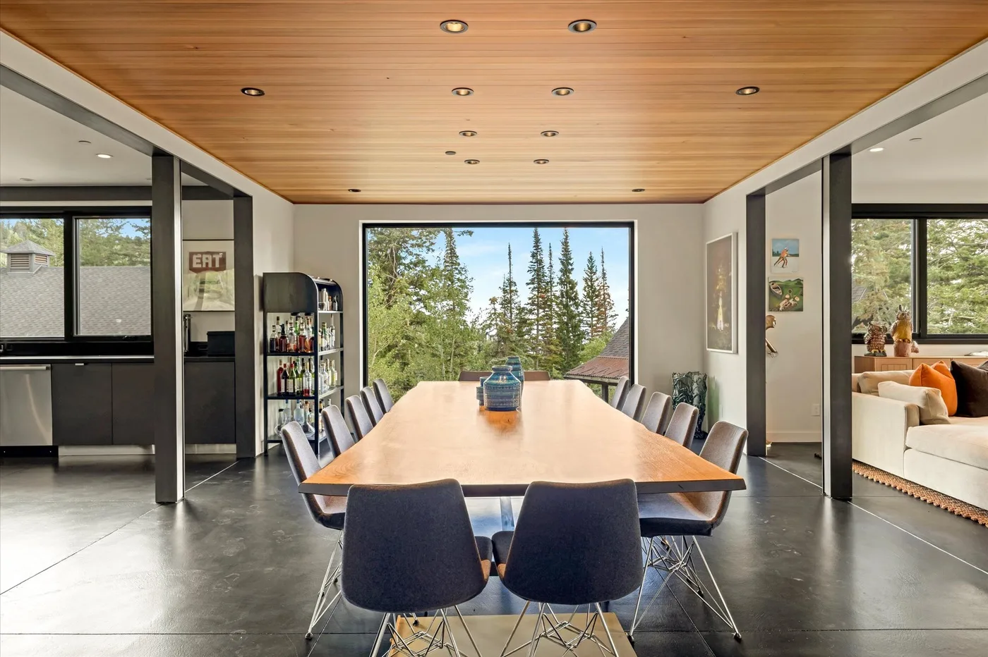 A long dining table fills a bright room with large windows and a wood ceiling.