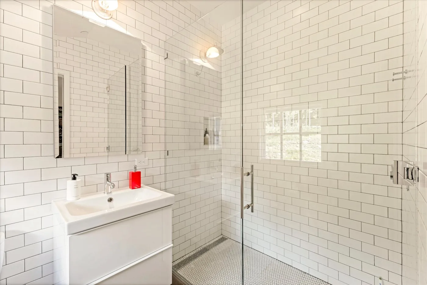 A bright tiled bathroom with a sink, mirror, and glass shower.