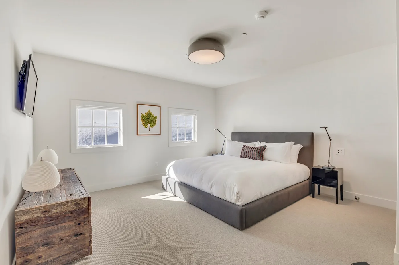 A bright bedroom with a large bed, two windows, and bedside tables.
