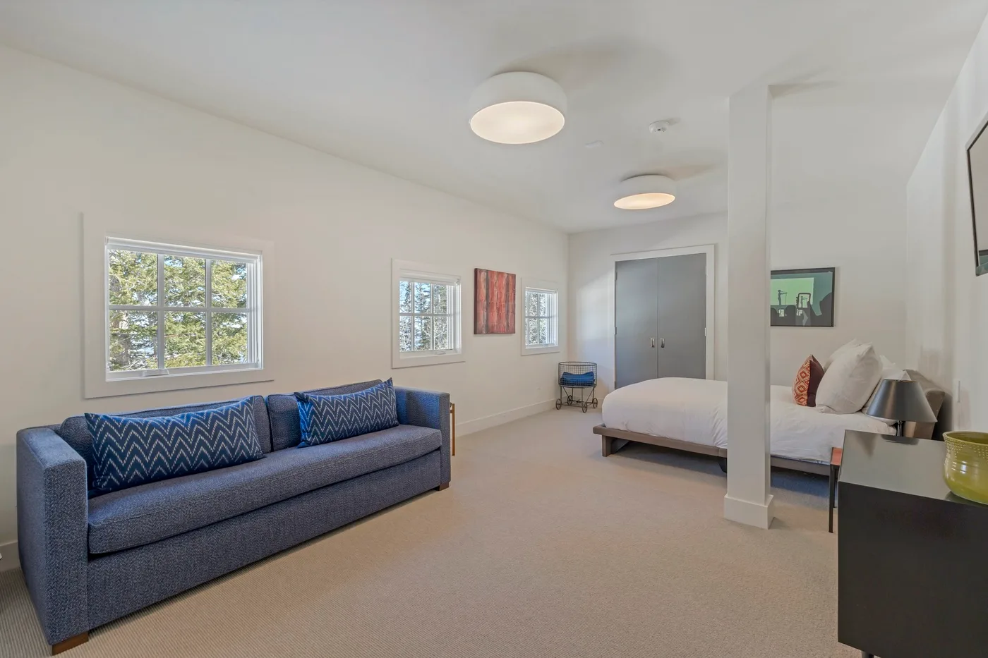 A bright bedroom with a blue seating area beside the bed and several windows.
