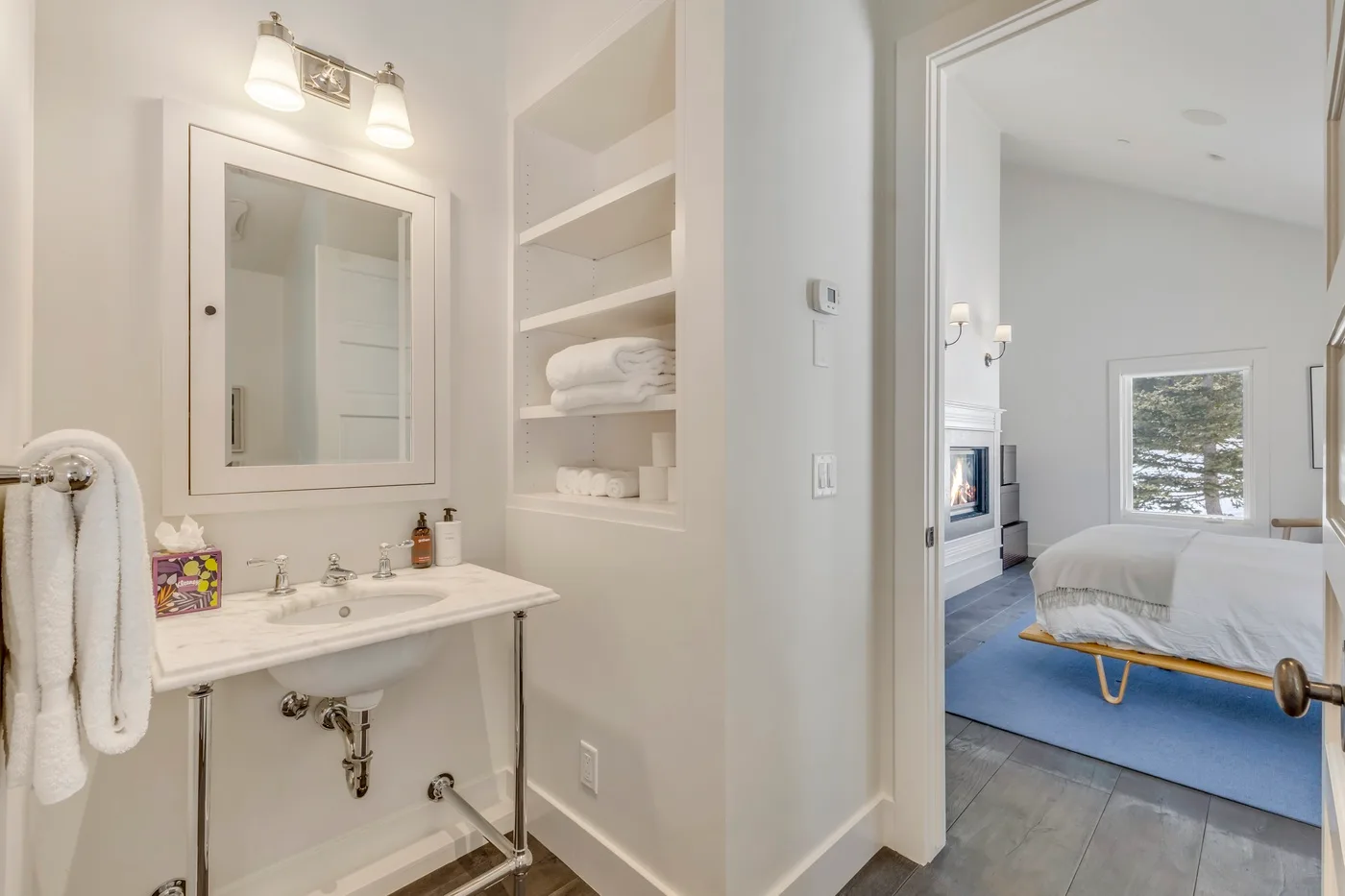 A bathroom with a sink and open shelves beside a bedroom.
