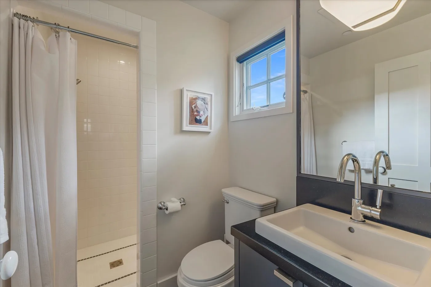 A bright bathroom with a shower, toilet, and sink beneath a window.