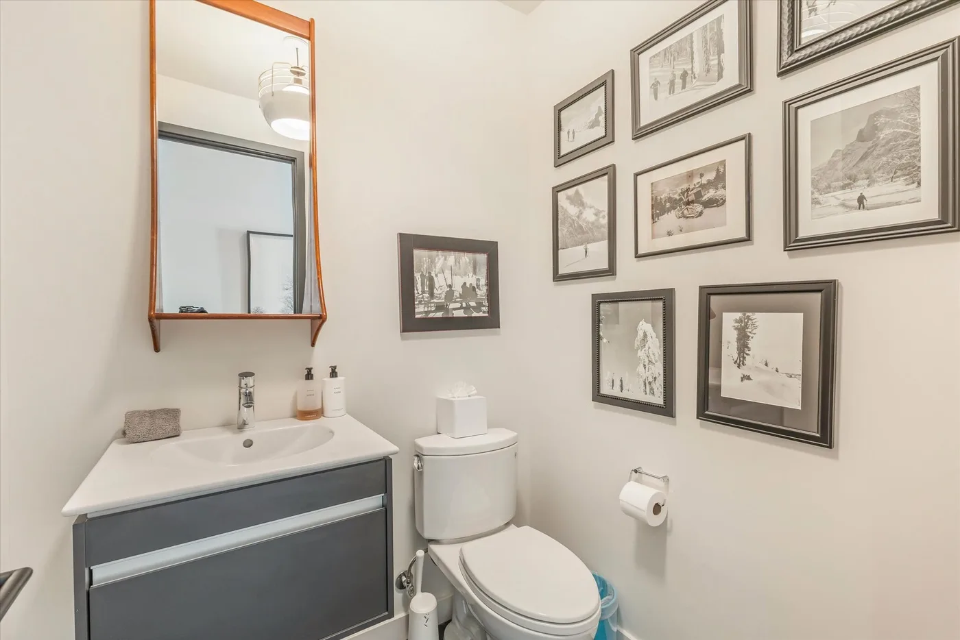A bathroom with a sink, toilet, and framed pictures on the wall.