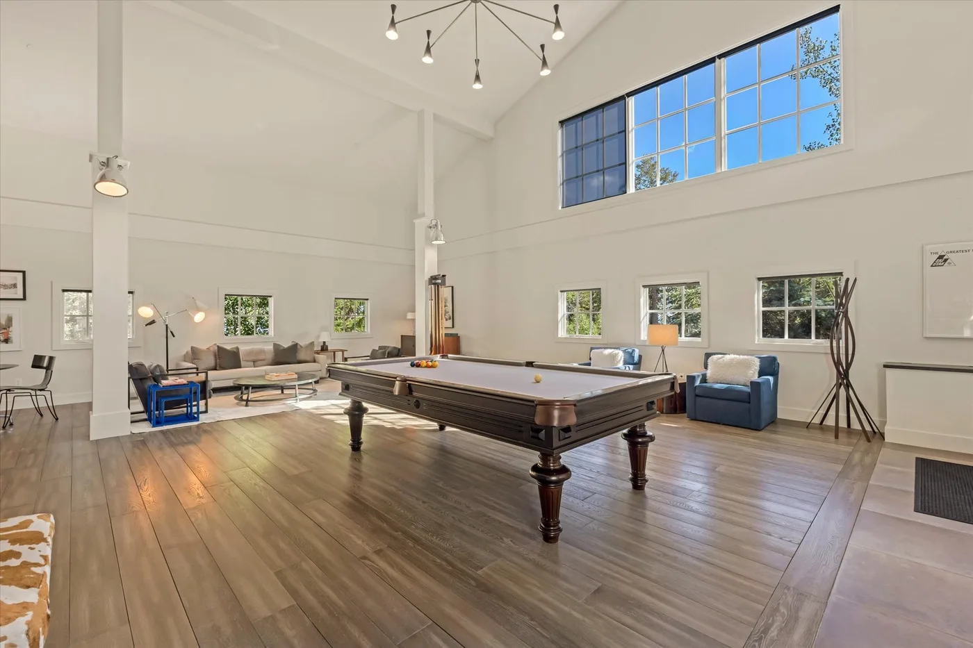 A bright game room with a pool table, seating, and large windows.