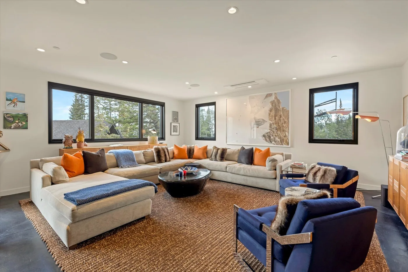 A bright living room features sectional seating, blue armchairs, and large windows.