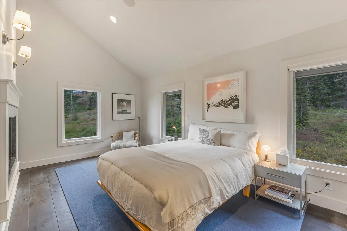 A bright bedroom with a bed, bedside tables, and windows overlooking greenery.