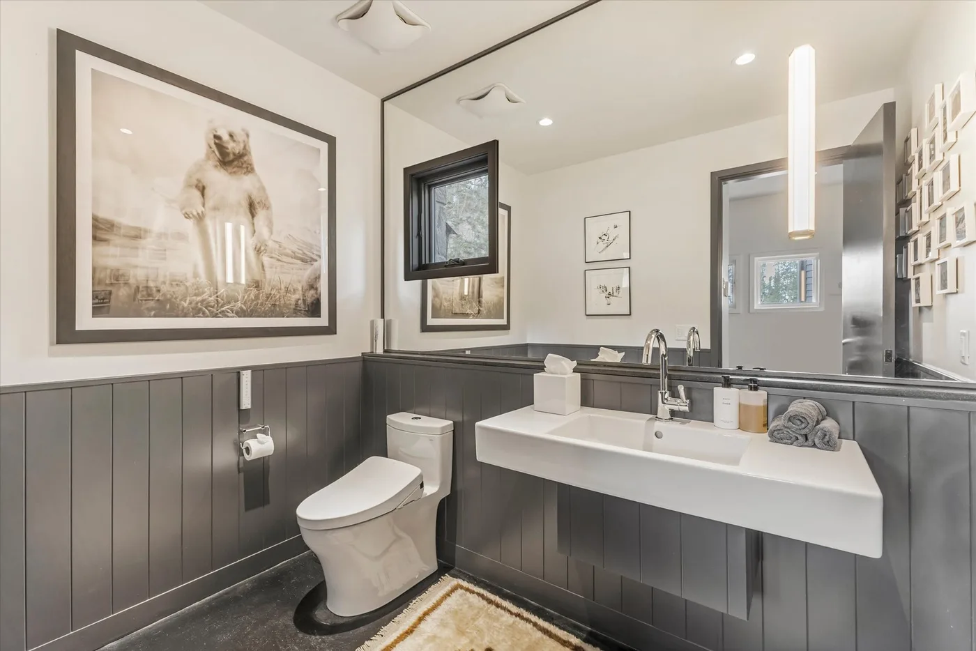 A modern bathroom with a wall-mounted sink, toilet, and framed artwork.