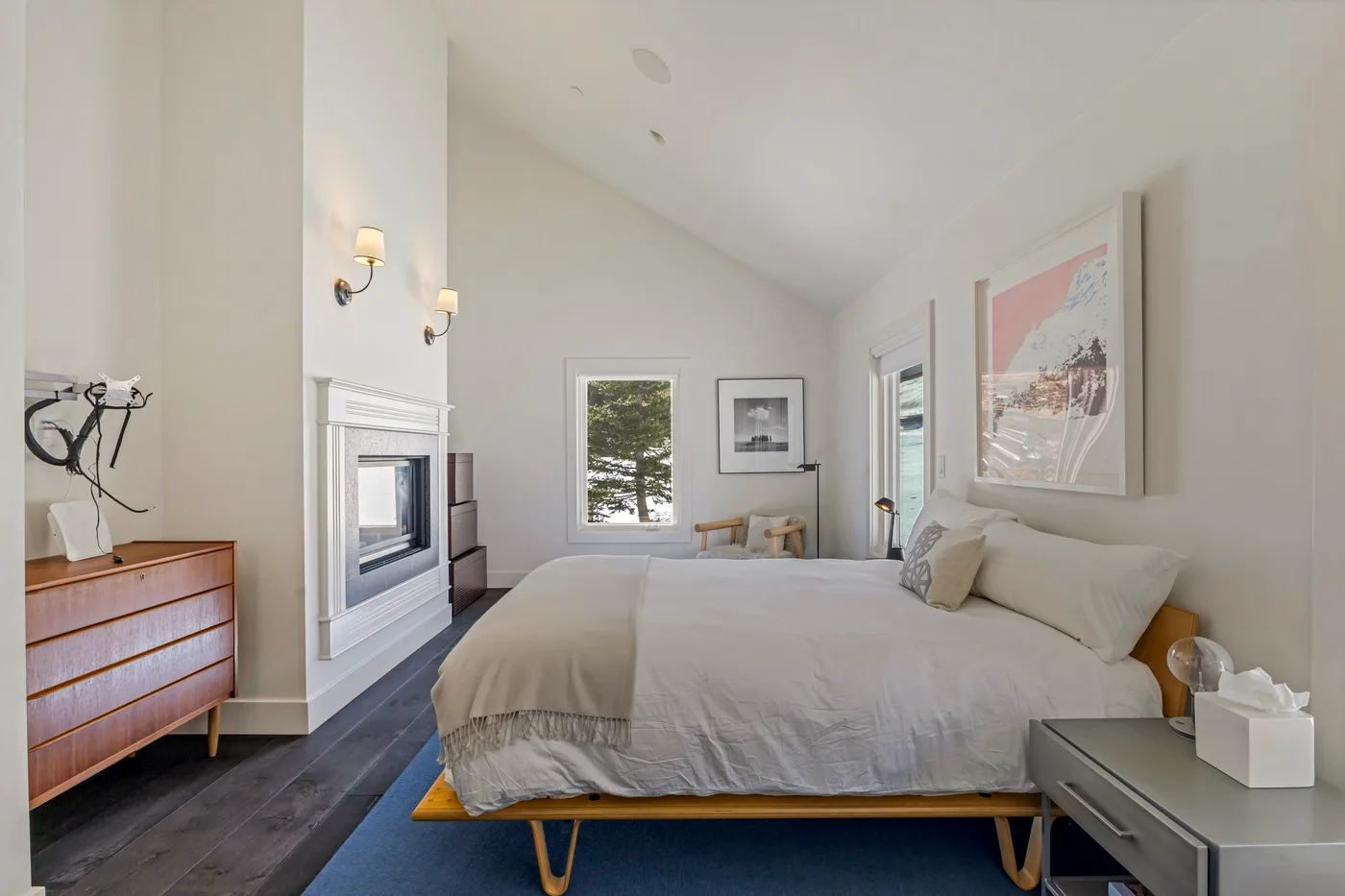 A bright bedroom with a large bed, framed artwork, and a fireplace.