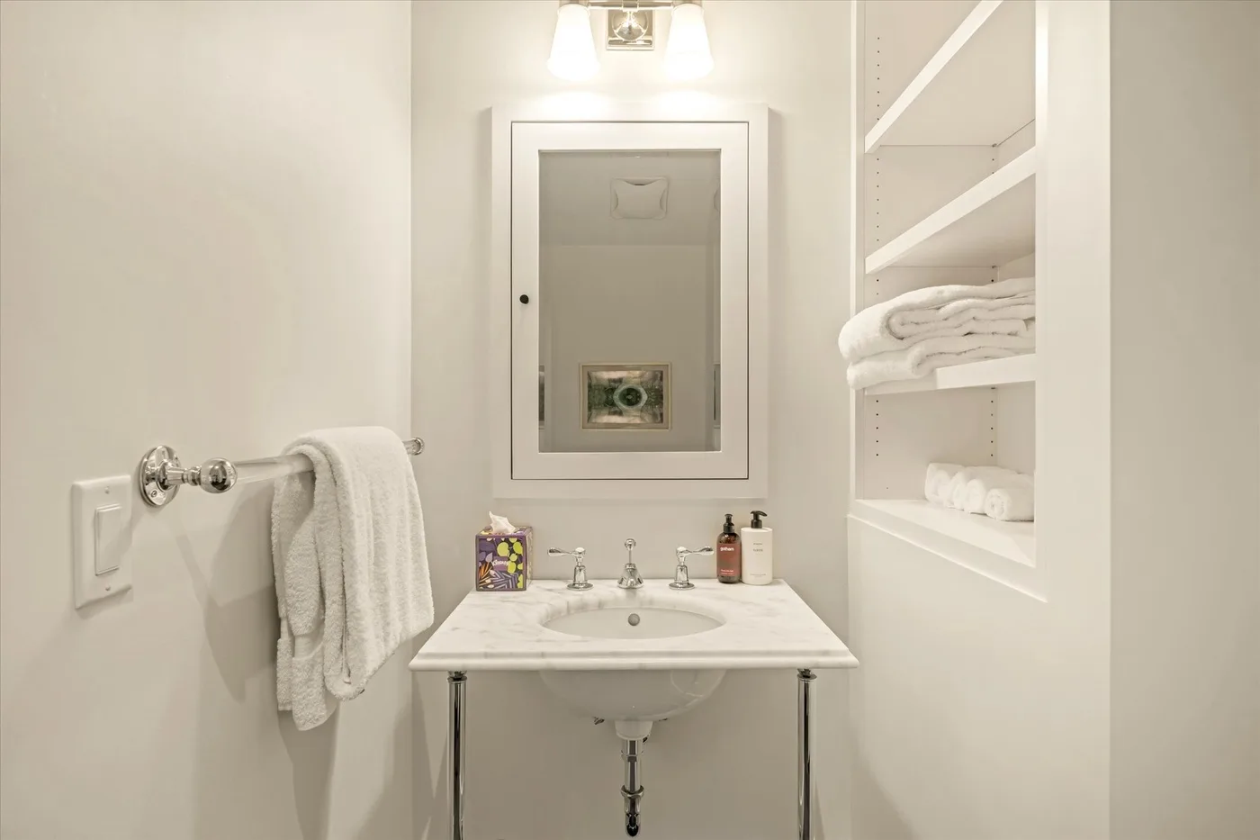 A bright bathroom vanity with a mirror, sink, and open towel shelves.