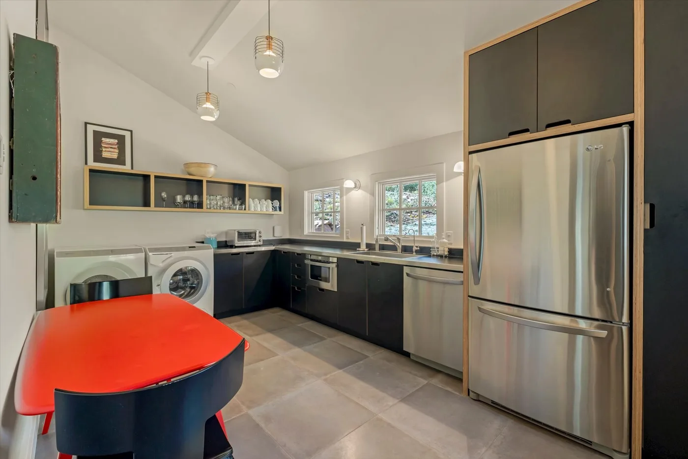 A modern kitchen with dark cabinets, stainless steel appliances, and a red countertop.