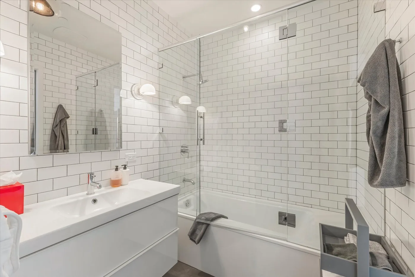 A tiled bathroom with a sink, bathtub, and glass shower screen.