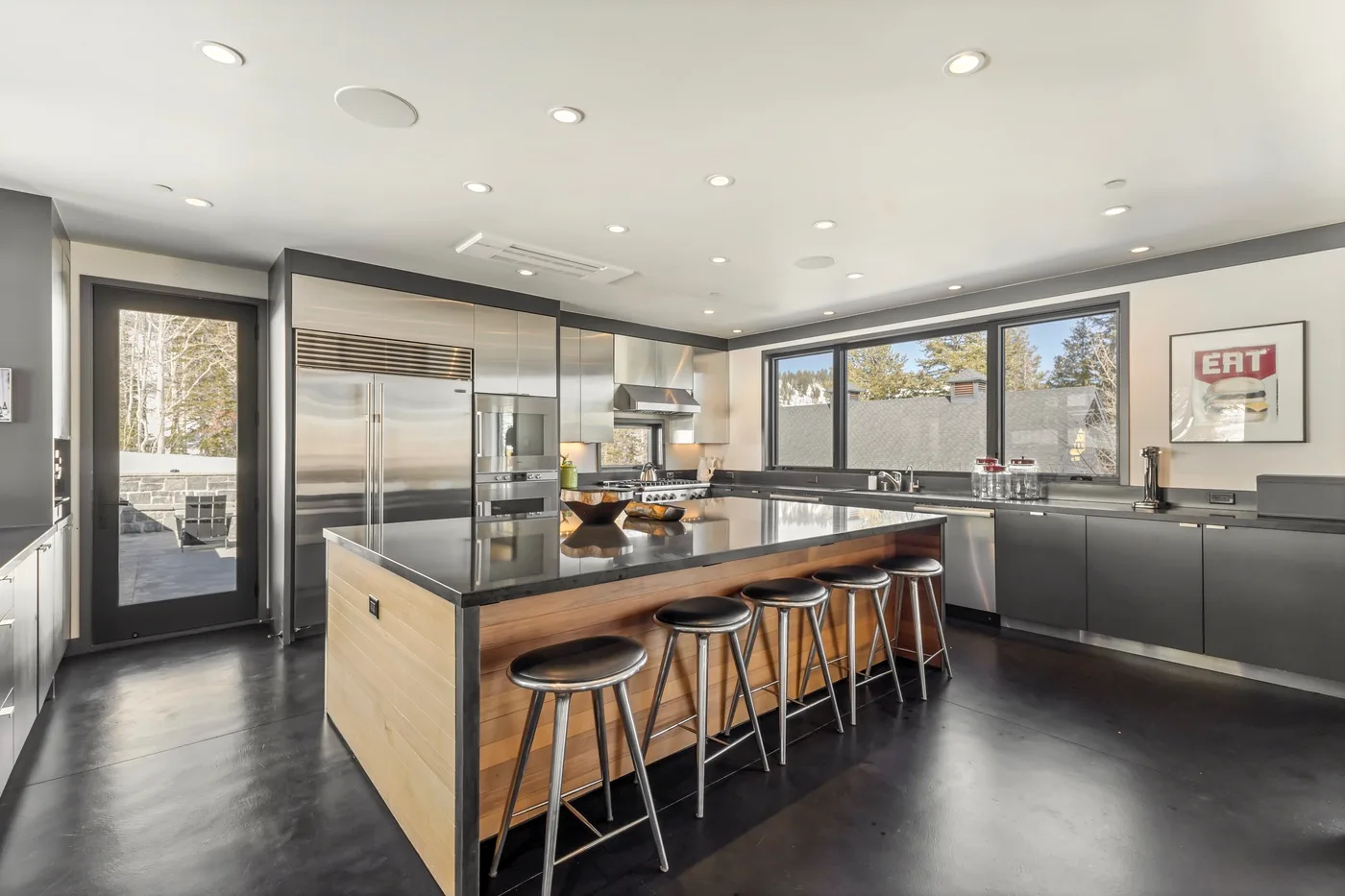 A modern kitchen with a large island and bar seating beneath wide windows.