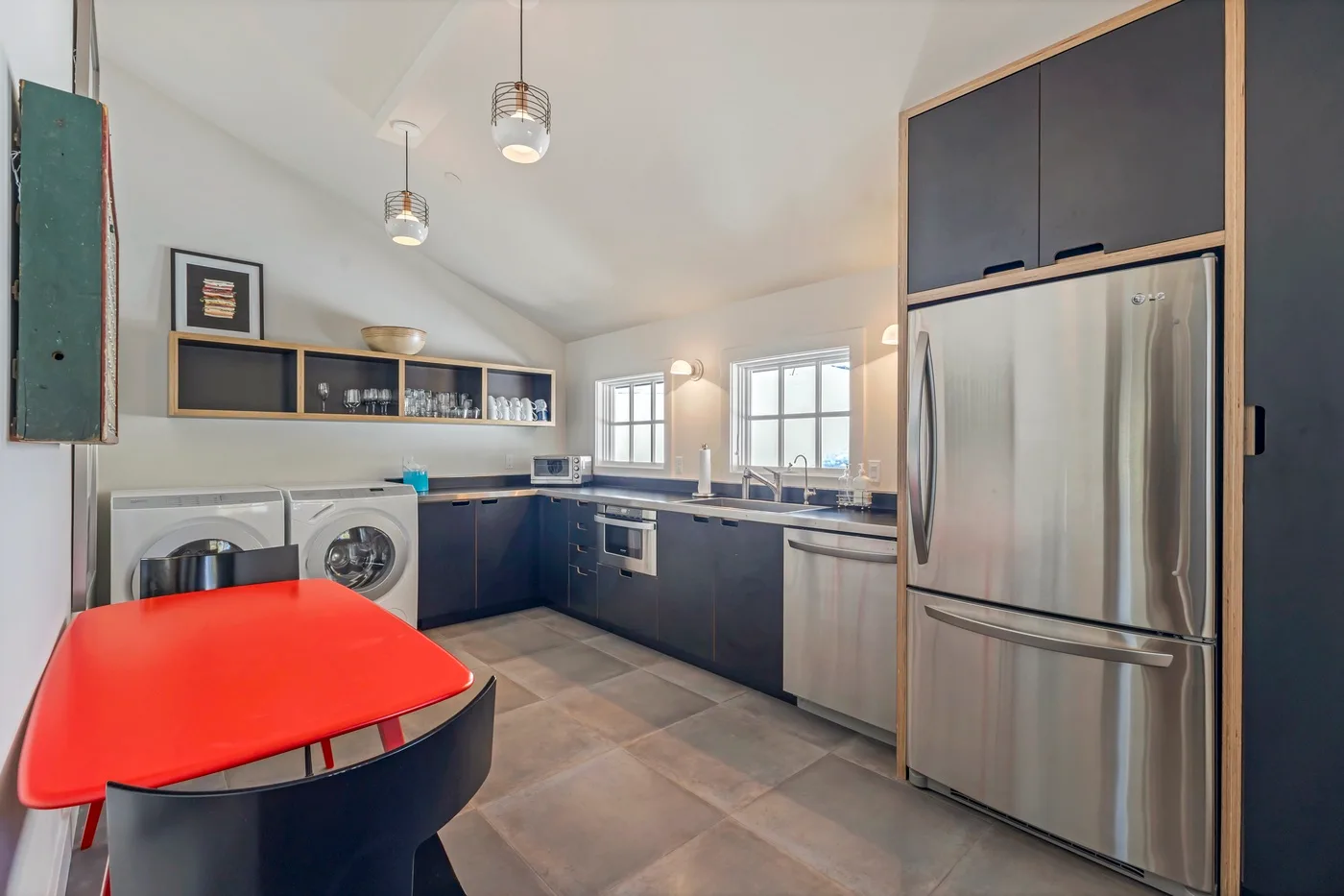 A bright kitchen with dark cabinetry, stainless steel appliances, and a red table.