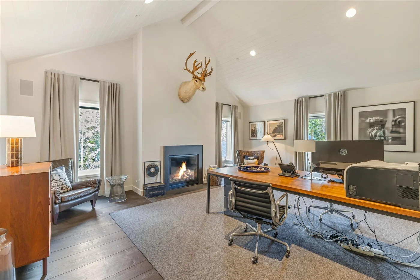 A bright home office with a long desk, computer monitors, and a fireplace.
