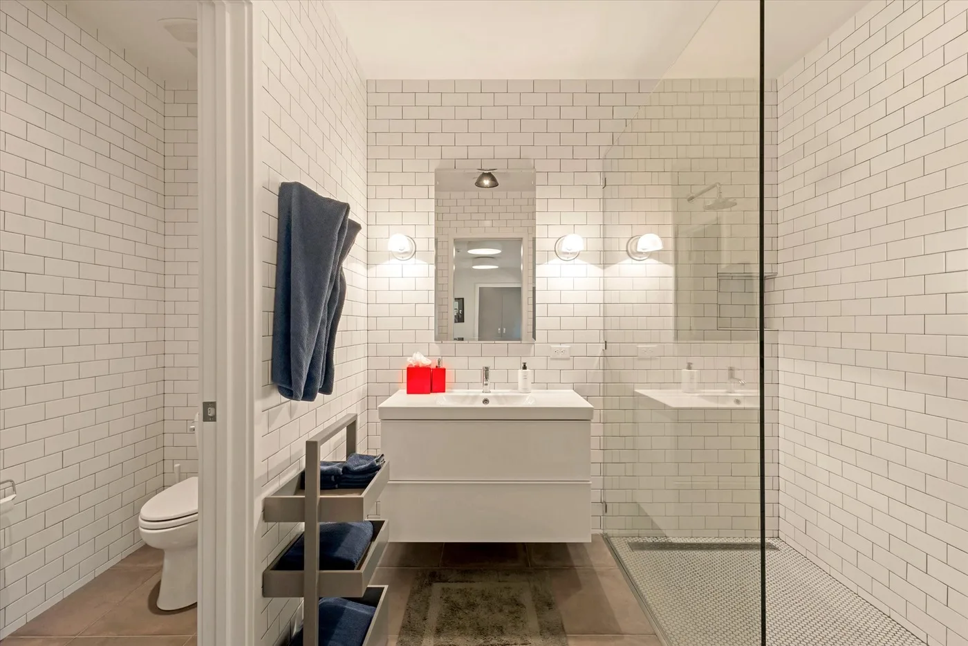 A tiled bathroom with a sink vanity, toilet, and glass shower.