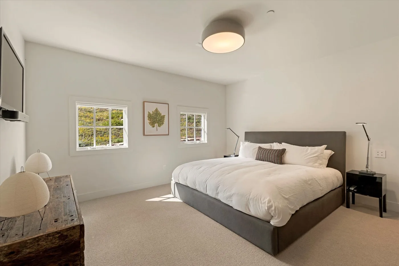 A bright bedroom with a large bed and windows along the wall.