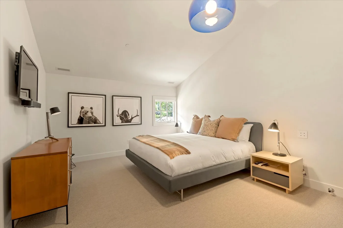 A bedroom with a low bed, framed artwork, and a window.