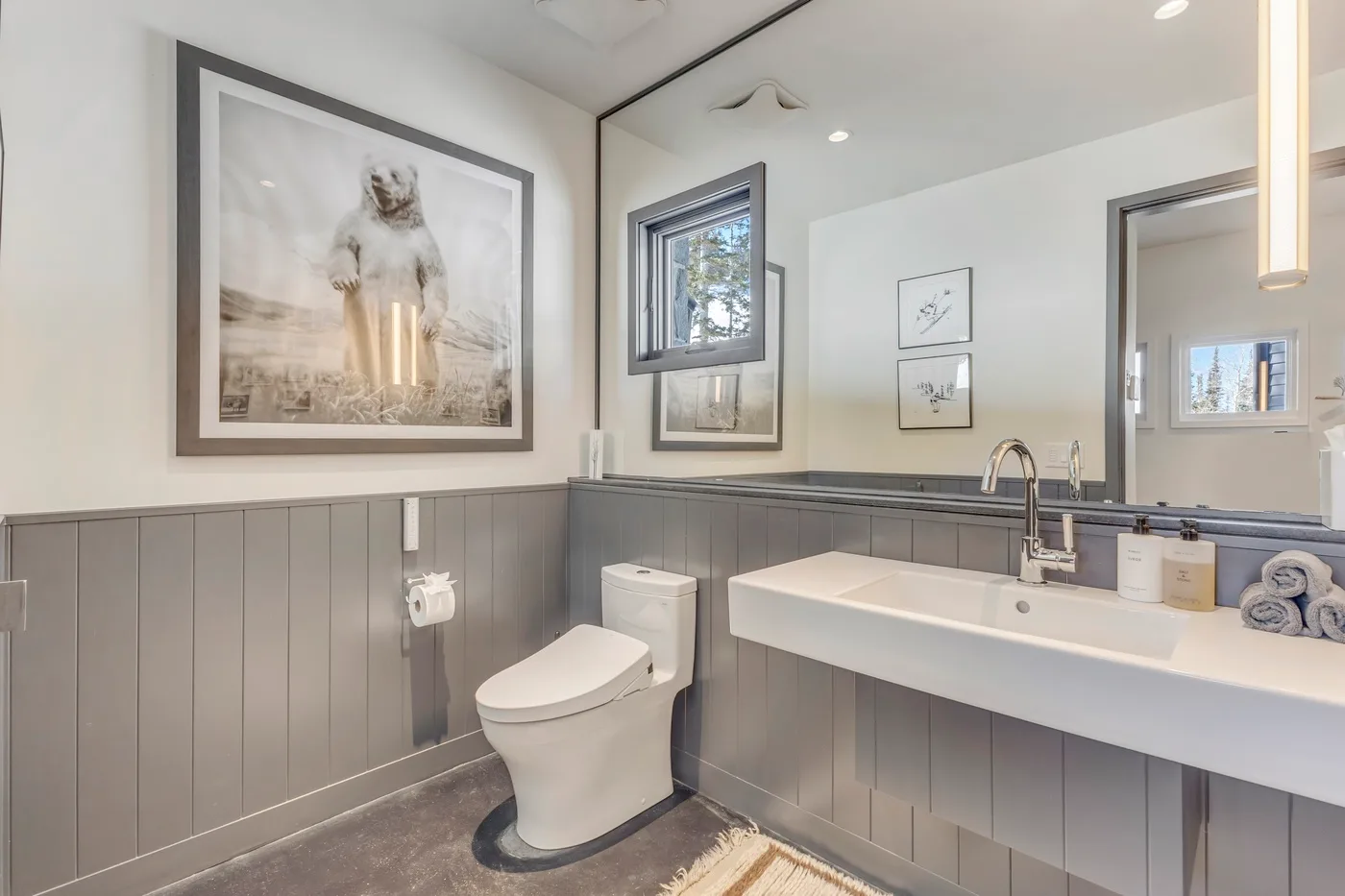 A bathroom with a toilet and a long sink beneath a mirror.