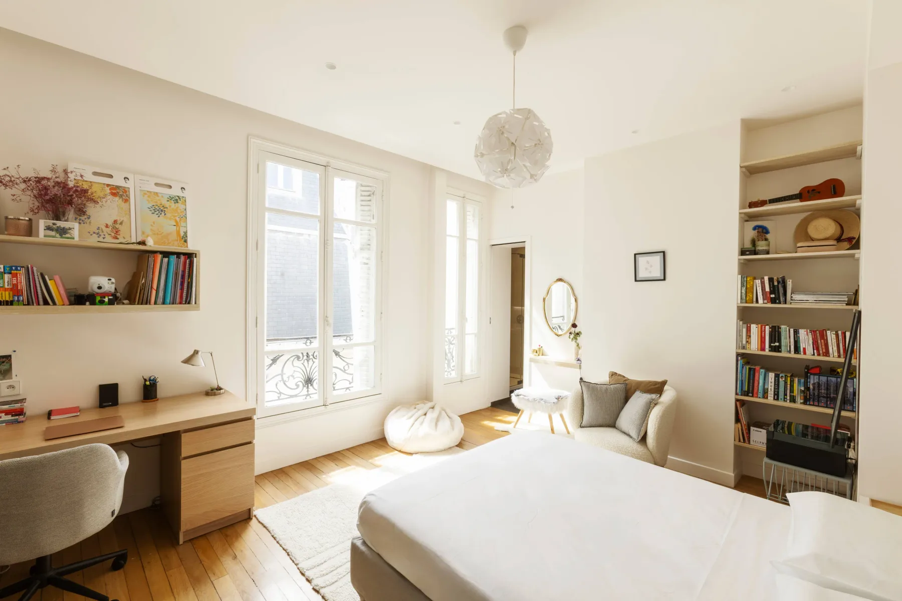A bright bedroom with a bed, desk, and tall windows.