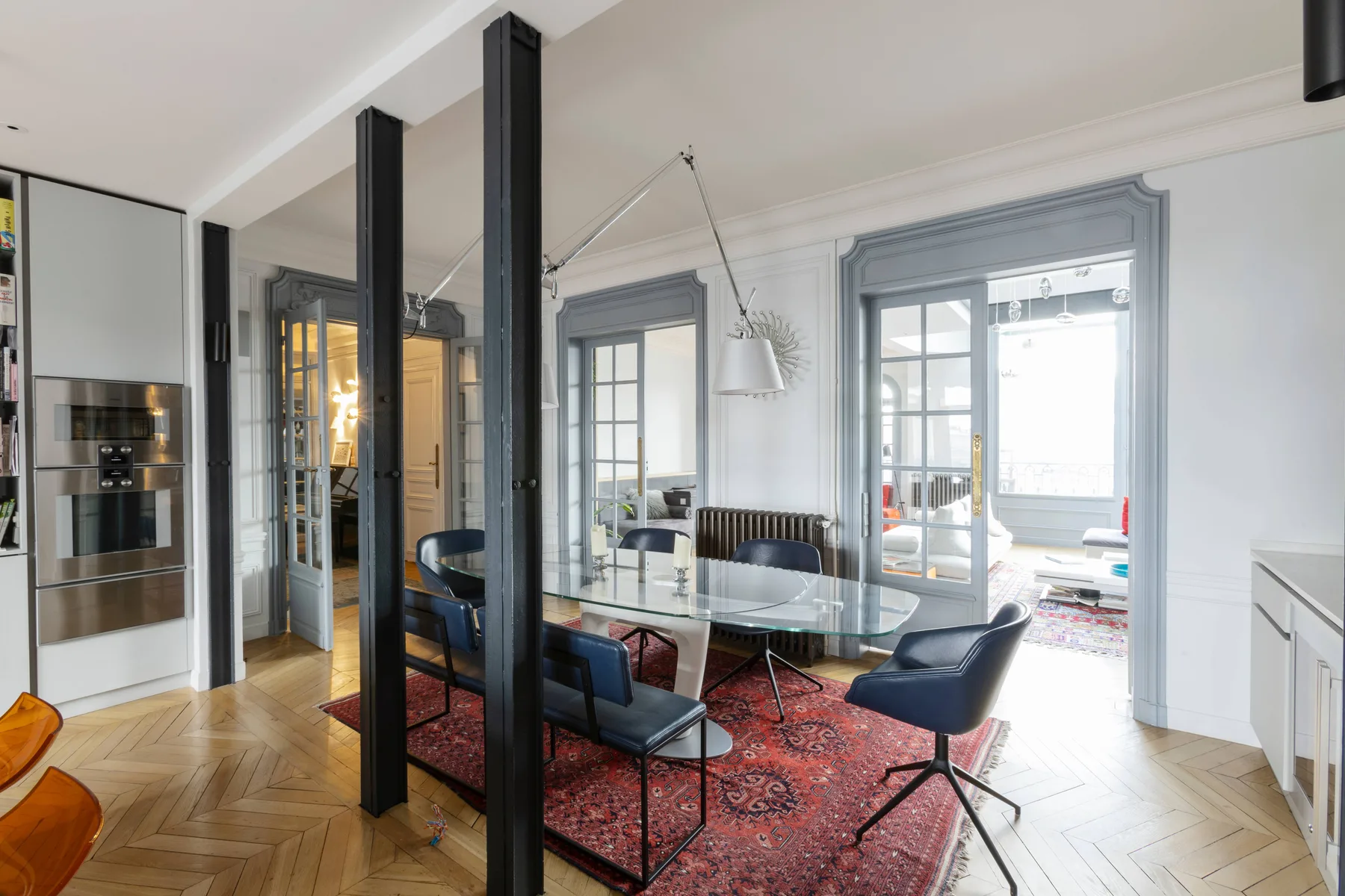 A dining area with a glass table and dark seating on a patterned rug.