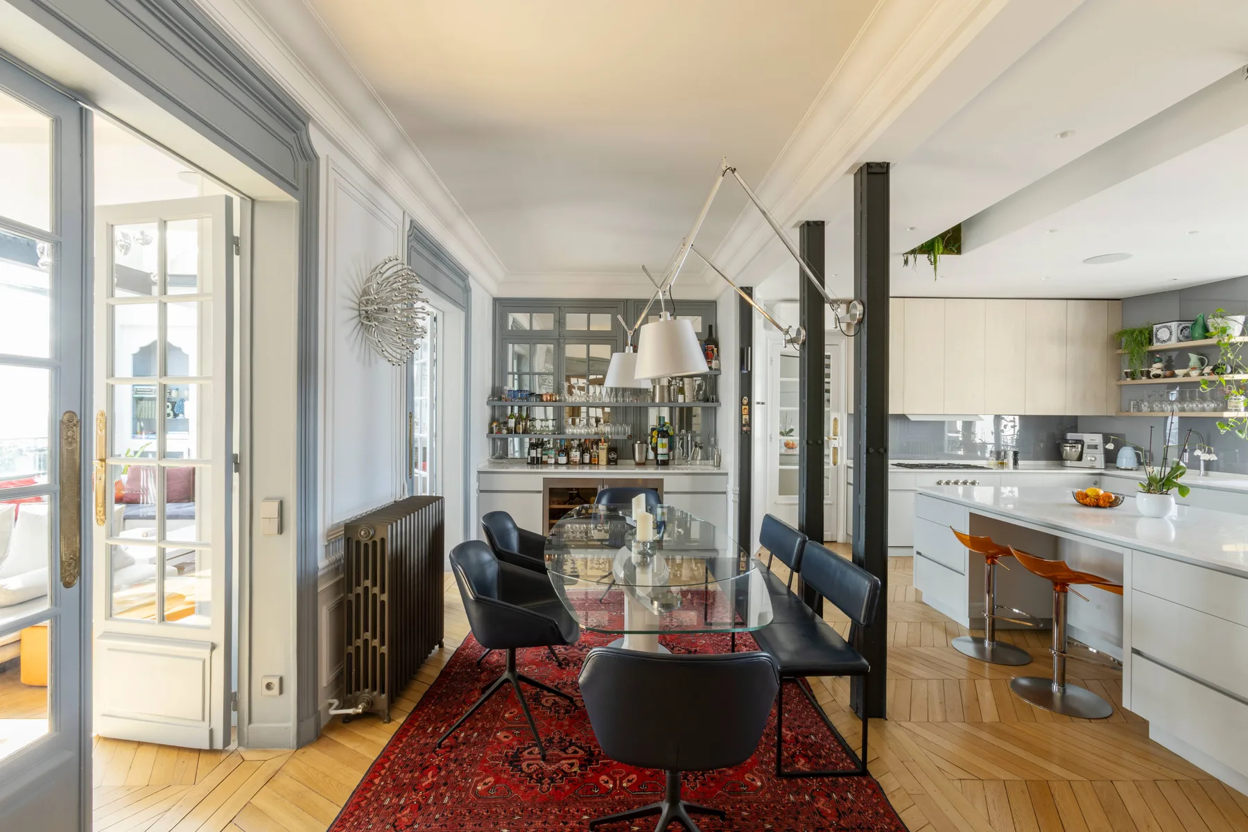 A dining area with a glass table and dark chairs opens onto a kitchen.