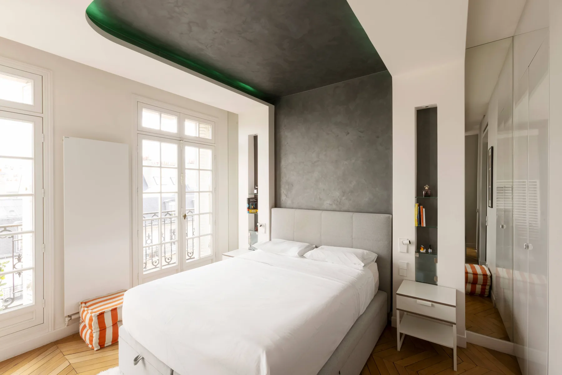 A bright bedroom with a white bed beside tall windows.