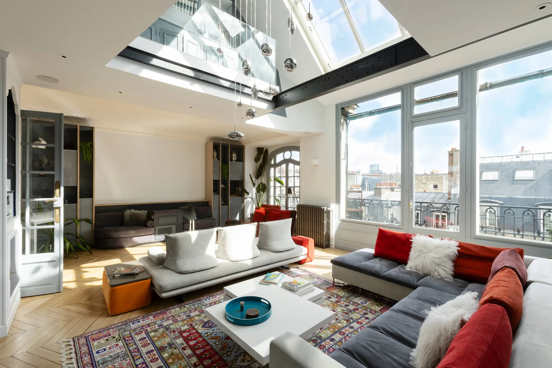 A bright living room with seating beneath a glass skylight and large windows.