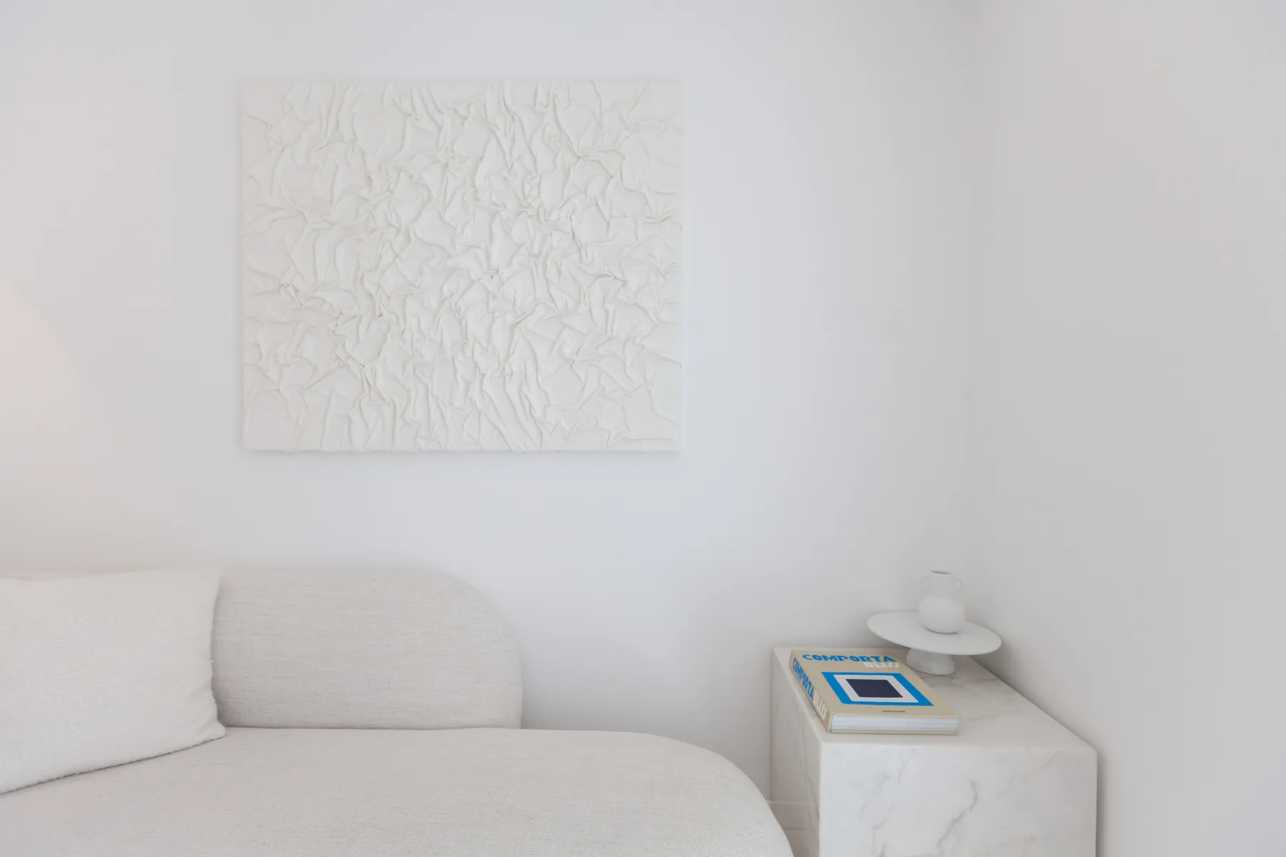 Una sala luminosa con asientos claros, arte mural texturizado y una mesa auxiliar pequeña.