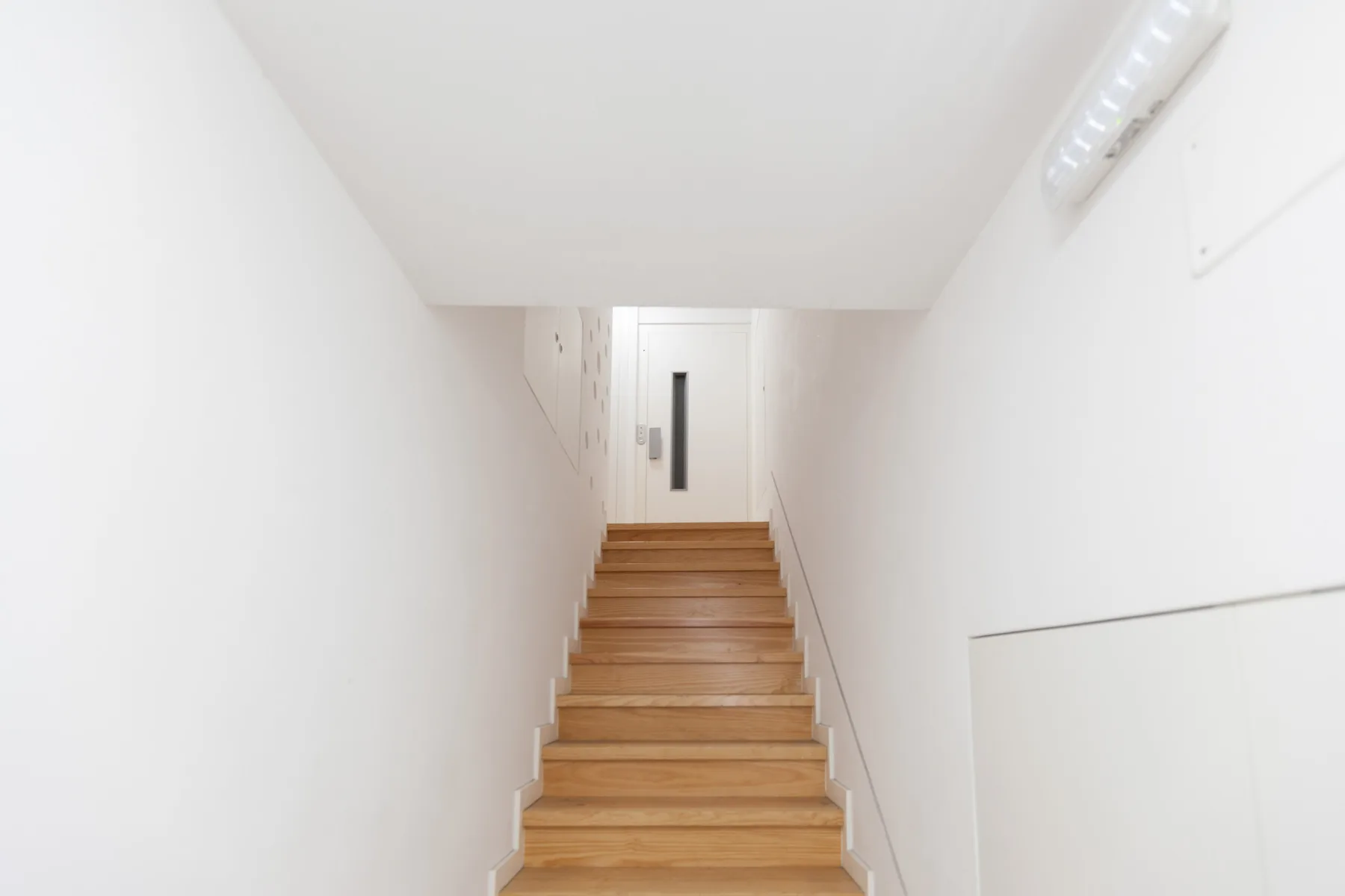 Una estrecha escalera blanca con peldaños de madera que conducen a una puerta.