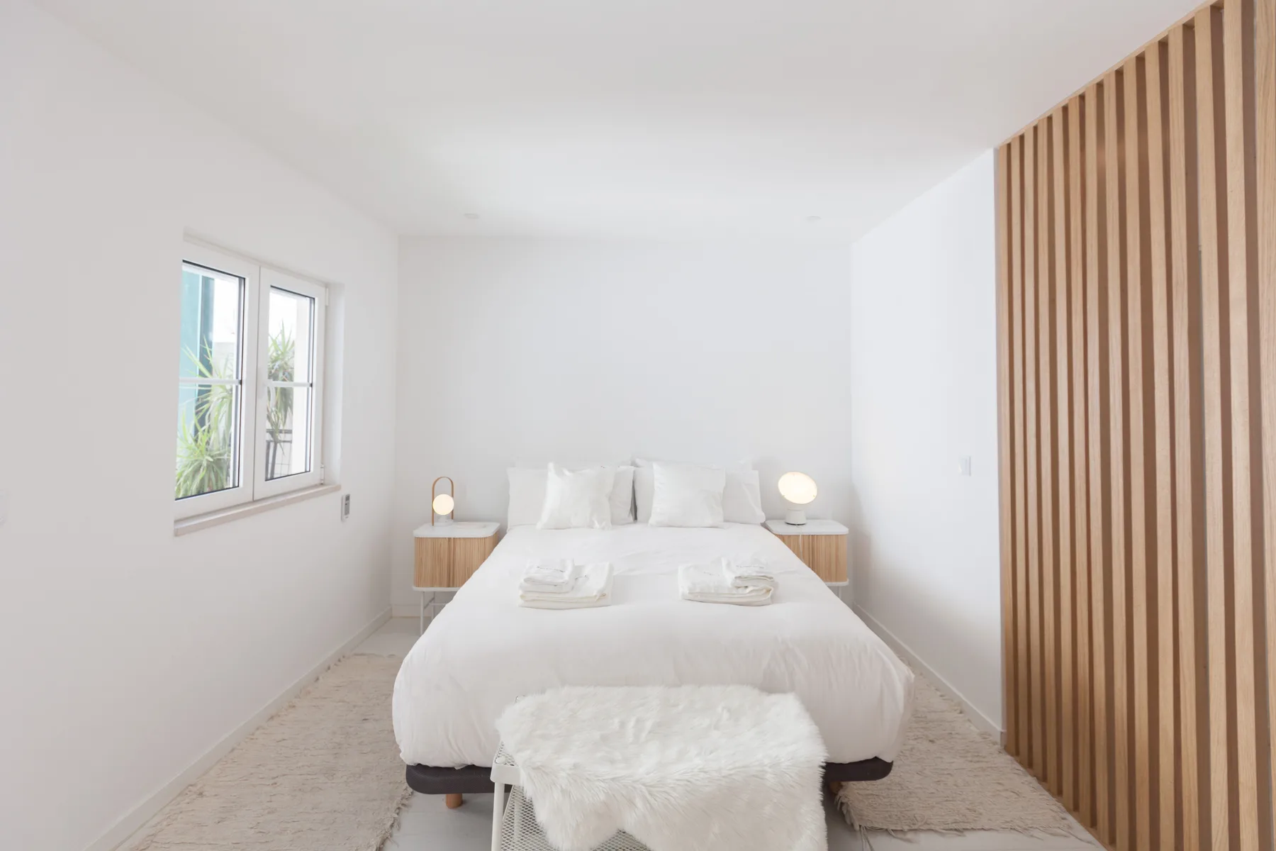 Un dormitorio luminoso con una cama blanca, mesas de noche y una ventana.
