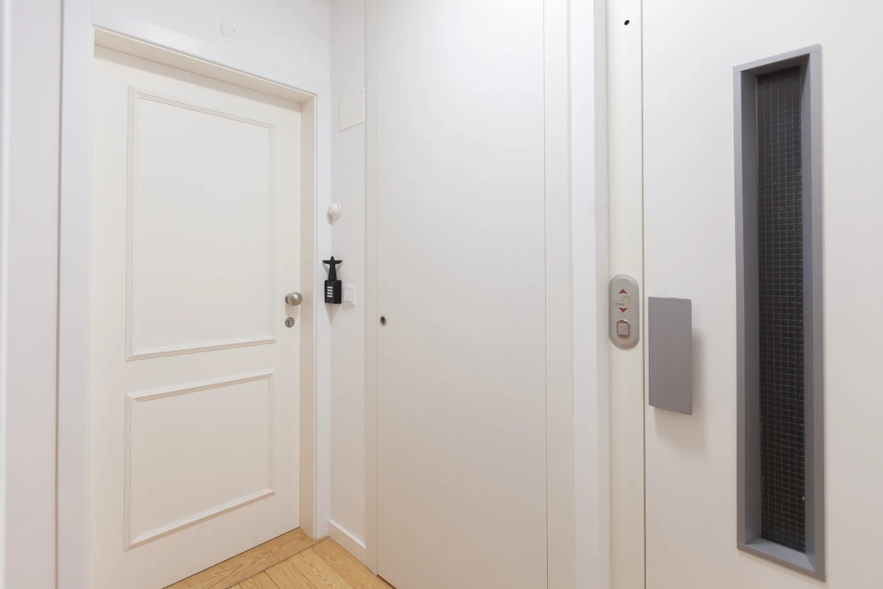 Una entrada luminosa con una puerta blanca y una ventana estrecha y oscura.