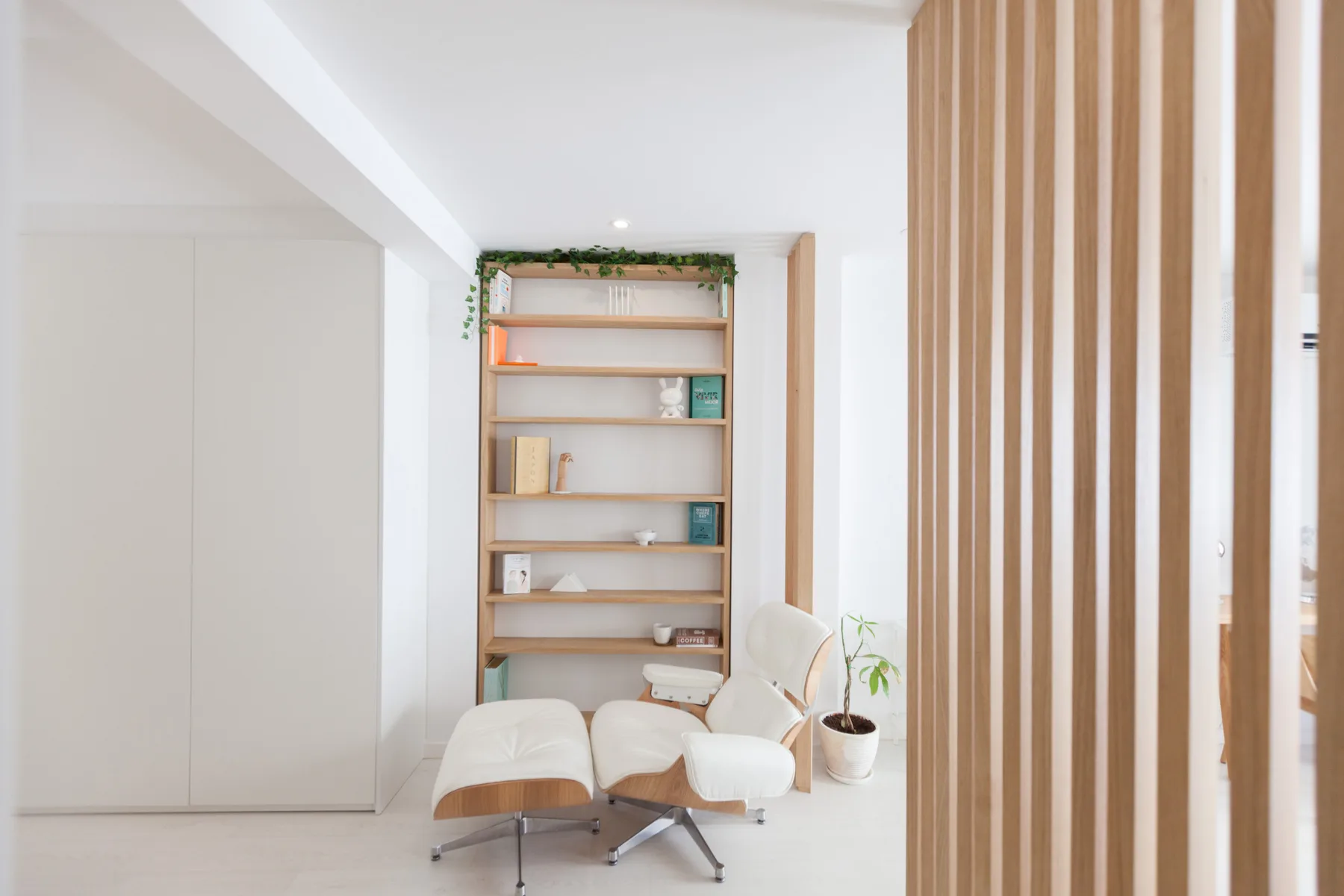 Una sala luminosa con un sillón junto a estanterías abiertas y una planta en maceta.