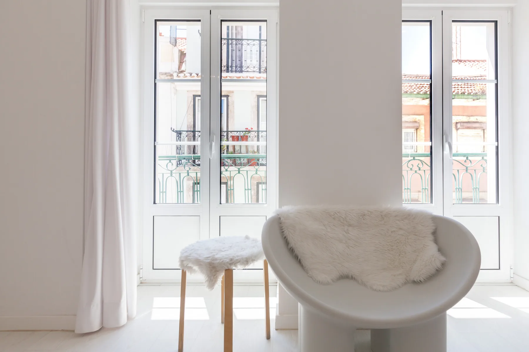 Una zona de estar luminosa con un sillón blanco junto a ventanas altas.